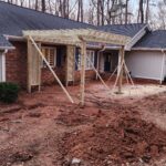 Front yard of a brick house under renovation, with a wooden pergola frame and braces