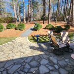 Stone patio with outdoor seating set and curved path through natural area in front yard.