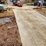 Construction workers pour concrete from a mixer truck into wooden forms for a new driveway
