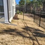 Backyard scene with sliding glass door on a beige house, a black metal fence.