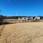 Back yard, black metal fence in the foreground and row of gray houses under a clear blue sky