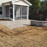 Gray paver patio, and a curved stone retaining wall by a black metal fence.